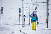 Young male skier walking at a snow-covered railroad track, Andermatt, Uri, Switzerland