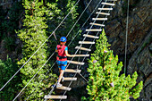 Woman crossing gorge on suspension bridge, Obergurgler Klettersteig, fixed-rope route, Obergurgl, Oetztal Alps, Tyrol, Austria