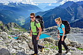 Man and woman hiking over boulders, ski area Presena and valley Val di Sole in background, Adamello-Presanella Group, Trentino, Italy
