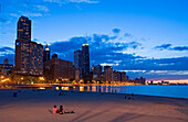 USA, Illinois, Chicago, Gold Coast und Gebäude auf dem Sand am Rande des Michigan-See bei Sonnenuntergang von Olive Park, Paar gesehen sitzt
