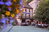 View through flowers to people in beer garden of Waldschloss Braeu brewery, Frammersbach, Spessart-Mainland, Bavaria, Germany