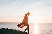 Silhouette of Caucasian woman walking on rocks at ocean