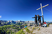 Three persons standing at cross at summit of Mondscheinspitze, Karwendel range in background, Mondscheinspitze, Natural Park Karwendel, Karwendel range, Tyrol, Austria