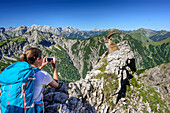 Woman hiking taking a photo of ibex, Karwendel range in background, Natural Park Karwendel, Karwendel range, Tyrol, Austria