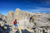 Frau beim Wandern liest Wegweiser, Pala di San Martino und Pala-Hochfläche im Hintergrund, Cima la Fradusta, Val Canali, Pala, Dolomiten, UNESCO Weltnaturerbe Dolomiten, Trentino, Italien
