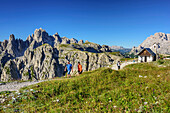 Mehrere Personen wandern an Kapelle vorbei, Cadinigruppe im Hintergrund, Paternsattel, Sextener Dolomiten, Dolomiten, UNESCO Weltnaturerbe Dolomiten, Südtirol, Italien