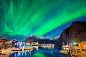 Aurora borealis, Polarlicht über Meeresbucht mit beleuchteten Booten und Häusern von Hamnoy, Hamnoy, Lofoten, Norland, Norwegen