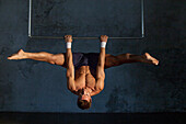 Gymnast with bare upper body doing an upside-down straddle, Germany