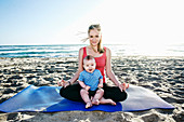 Lächelnde Mutter macht Yoga am Strand mit ihrem kleinen Sohn