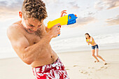 Caucasian couple playing with squirt guns on beach