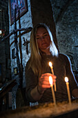Young woman lighting a candle in a small church, Gudauri, Mtskheta-Mtianeti, Georgia