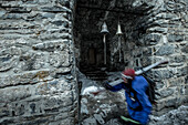 Junge Skifahrerin läuft an kleinen Glocken einer Ruine vorbei, Gudauri, Mzcheta-Mtianeti, Georgien