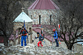 Three young skiers walking past a church in a village, Gudauri, Mtskheta-Mtianeti, Georgia