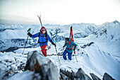 Zwei junge Skifahrer steigen durch den Tiefschnee auf den Gipfel eines Berges, Gudauri, Mzcheta-Mtianeti, Georgien
