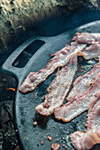 Close up of a frying pan on a campfire with roasted bacon, Lake Vaner, Vastergotland, Sweden