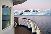 Deck von Expeditions Kreuzfahrtschiff MV Sea Spirit (Poseidon Expeditions) vor Eisberg und schneebedeckten Bergen in der Abenddämmerung. Paradise Harbor (Paradise Bay), Danco-Küste, Grahamland, Antarktische Halbinsel, Antarktis