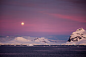 Full moon over snow-covered mountains at dusk near Lemaire Channel, Graham Land, Antarctic Peninsula, Antarctica