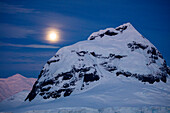 Full moon over snow-covered mountain at night near Lemaire Channel, Graham Land, Antarctic Peninsula, Antarctica