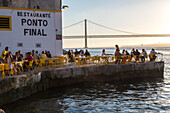 riverfront restaurant Ponto Final, view from south bank of River Tagus,and the 25th April Bridge, Cacilhas, Almada, Lisbon, Portugal