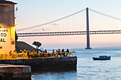 sunset on riverfront restaurant Ponto Final, view from south bank of River Tagus,and the 25th April Bridge, Cacilhas, Almada, Lisbon, Portugal