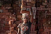 Ein junger Mann trägt bis zu 50 Kilo Ziegelsteine, indem er sie auf dem Kopf balanciert, Ziegelfabrik in Chittagong Hill Tracts, Bangladesch, Asien