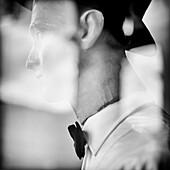 Old mannequin in shop window with hat and bow tie, reflections on glass