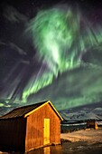 Northern Lights illuminates the wooden cabin at Lenangsoyra Lyngen Alps Tromsø Lapland Norway Europe.