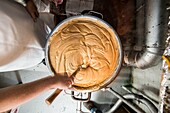 Overhead view of a person stirring peanut butter in a metal pot.