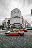 Kreuzung mit rotem Taxi am Ginza Place an wolkigem Tag, Chuo-ku, Tokio, Japan