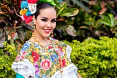 Female teenager, wearing folkloristic Mexican outfit, smiling at camera.