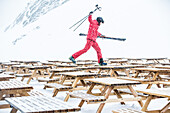 Young male skier walking over tables from a restaurant in the mountains, Kaprun, Salzburg, Austria