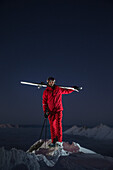 Junger Skifahrer steht auf dem Gipfel eines Berges über den Wolken bei Nacht, Kaprun, Salzburg, Österreich