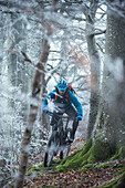 Young man riding with his bike through a with frost covered forest, Allgaeu, Bavaria, Germany