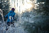 Junger Mann läuft durch einen mit Frost bedeckten Wald, Allgäu, Bayern, Deutschland