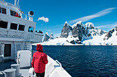 Passagier am Bug von Expeditions-Kreuzfahrtschiff MS Bremen (Hapag-Lloyd Cruises) vor der Bergformation Una Peaks, Lemaire-Kanal, nahe Grahamland, Antarktische Halbinsel, Antarktis