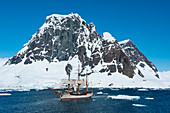 Segelschiff Europa (eine Bark) navigiert durch Eisschollen mit Berg im Hintergrund, Lemaire-Kanal, nahe Grahamland, Antarktische Halbinsel, Antarktis