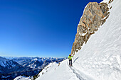 Frau auf Skitour steigt unter Felswand hindurch zur Rotwand auf, Bayerische Alpen im Hintergrund, Rotwand, Spitzing, Bayerische Alpen, Oberbayern, Bayern, Deutschland