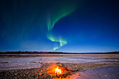 'The aurora forms the shape of an S above a makeshift campfire on the frozen braids of the Gerstle River near the Alaska Highway; Alaska, United States of America'