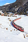 Red train of Rhaetian Railway passes in the snowy landscape of Arosa, district of Plessur, Canton of Graubunden, Switzerland, Europe