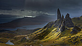 A burst of light briefly illuminates the pinnacles surrounding the Old Man of Storr against an approaching storm, Isle of Skye, Inner Hebrides, Scotland, United Kingdom, Europe
