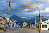 Colourful houses on touristic road framed by traffic lights post with snowy mountain chain beyond, Ushuaia, Argentina, South America