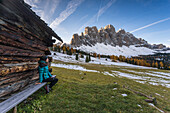 Girl sitting on a bench admiring the view of the GeislerVal di Funes, Trentino Alto Adige, Italy
