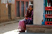 A woman relaxes in the sun, smoking his cigarette and observing the life around her, Panauti, Nepal