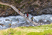 Hikers cross the wooden bridge on a creek Minor Valley High Valtellina Livigno Lombardy Italy Europe