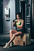 Young female boxer wrapping hand wrap while sitting at gym