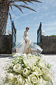 Portrait of happy bride standing at entrance with rose bouquet in background