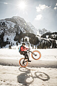 A young man performs a wheelie on a fatbike, snowbike, mountainbike  at Lauenensee near Gstaad, Bernese Oberland, Switzerland