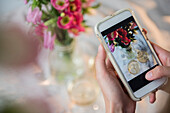 Caucasian woman photographing champagne and flowers with cell phone
