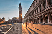 Europe, Italy, Veneto, Venice, People running in St, Mark's Square while the sun rises from behind the St, Mark bell tower