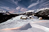 Waves of snow and huts in the small village of Andossi by Madesimo in a full moon night, Valchiavenna, Italy